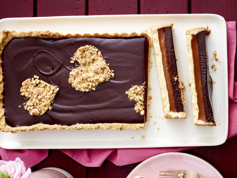 Schoko-Karamell-Tarte auf einem weißen Teller auf dunkelrotem Hintergrund.