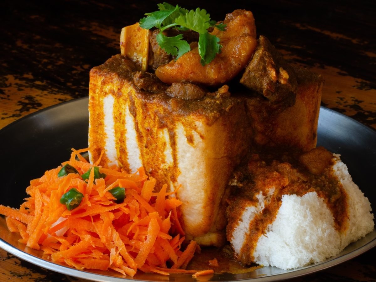 Südafrikanisches Bunny Chow: Ein ausgehöhltes Brot gefüllt mit Curry aus Fleisch und Kartoffeln, garniert mit Koriander, serviert mit scharfem Karottensalat.
