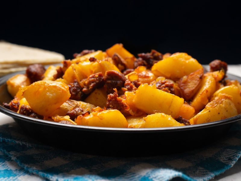 Ein schwarzer Teller mit der Chorizo-Kartoffelpfanne von der Seite fotografiert.