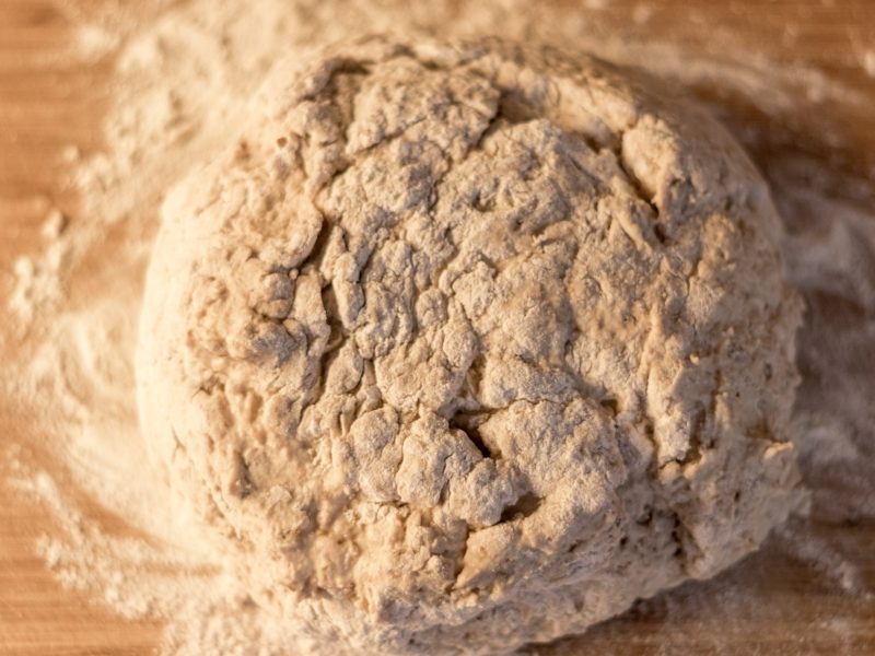 Draufsicht: Ein rund geformter Low-Carb-Pizzateig auf einer bemehlten Fläche aus Holz.