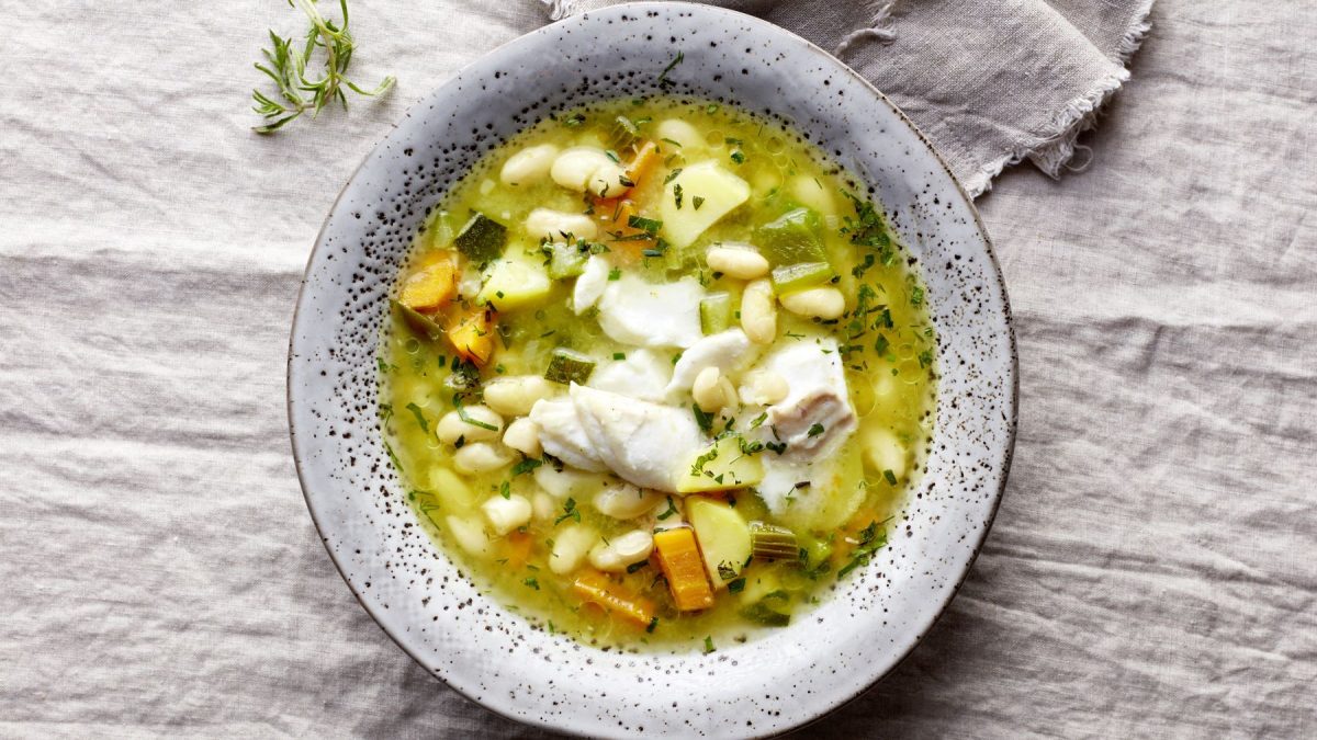 Bohnensuppe mit Skrei in einem grauen Suppenteller auf grauem HIntergrund.