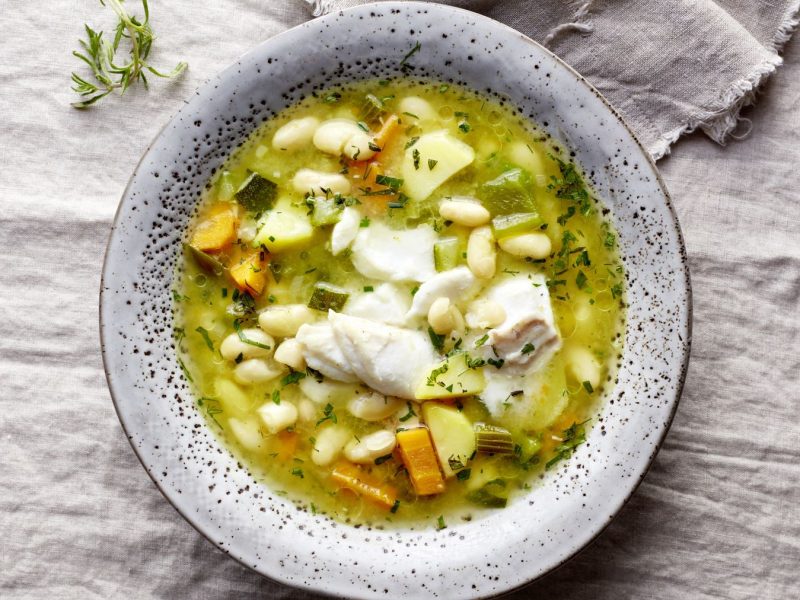 Bohnensuppe mit Skrei in einem grauen Suppenteller auf grauem HIntergrund.