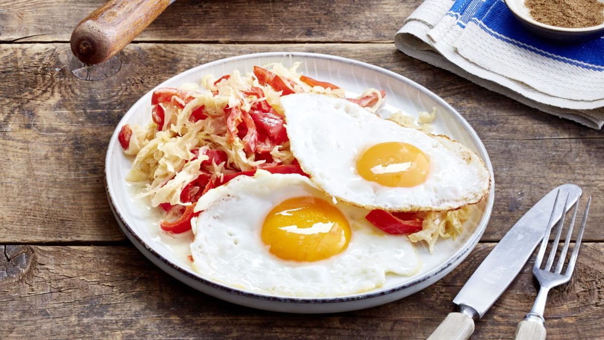 Sauerkraut-Pfanne mit Spiegelei auf einem weißen Teller auf hölzernem Hintergrund.