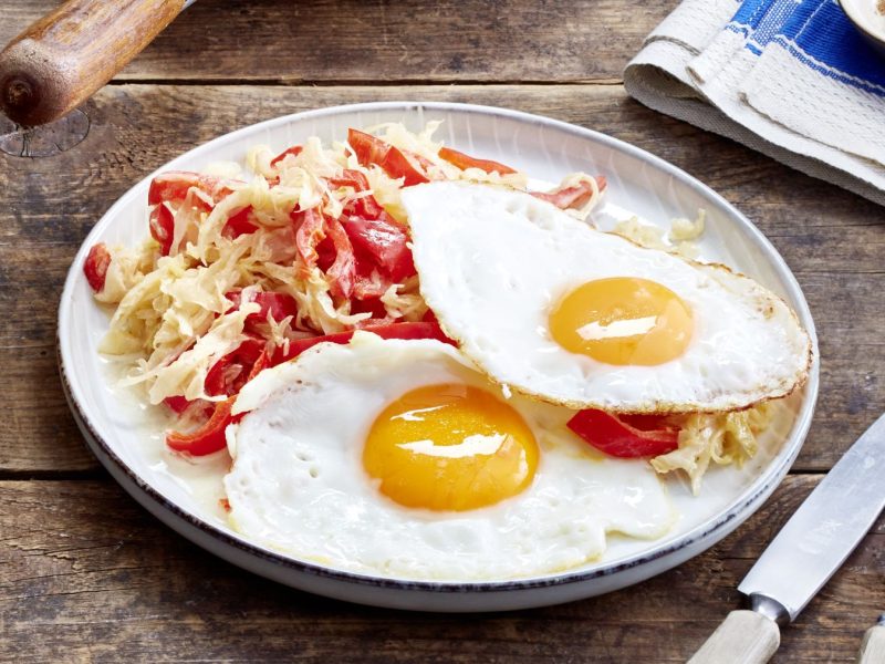 Sauerkraut-Pfanne mit Spiegelei auf einem weißen Teller auf hölzernem Hintergrund.