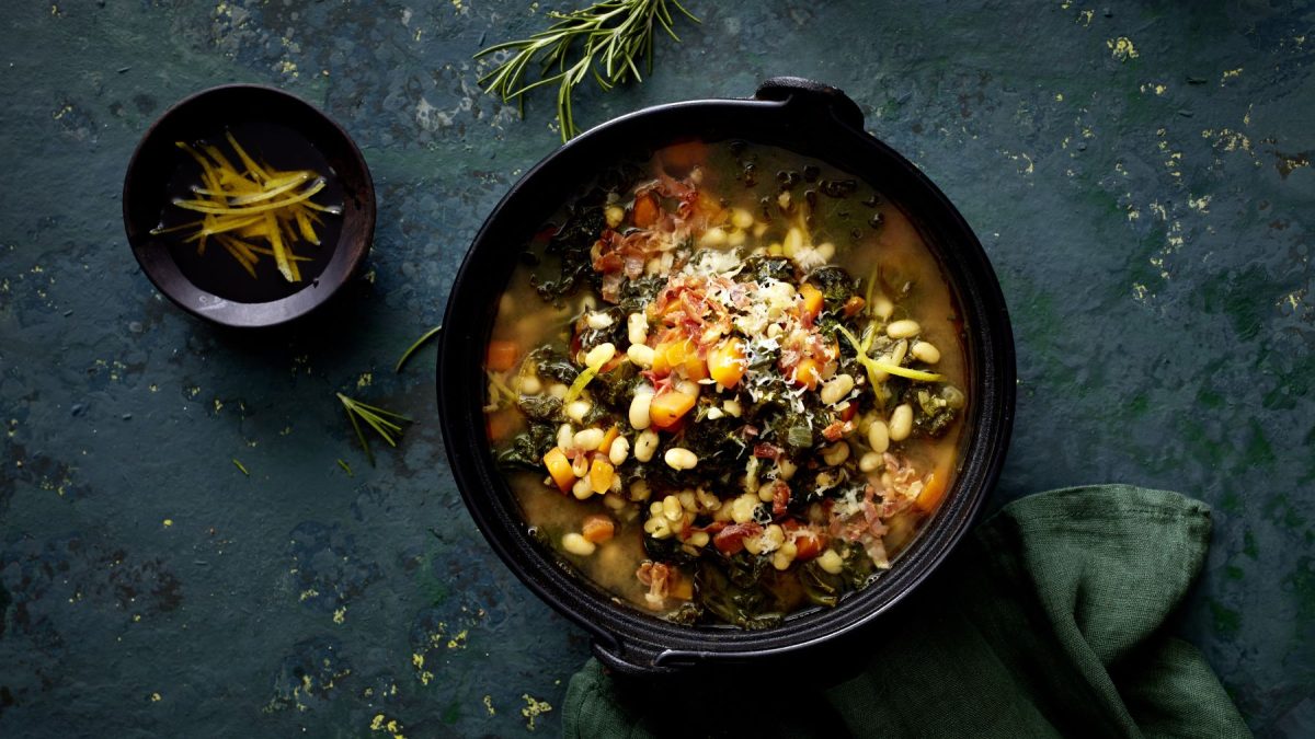 Toskanische Ribollita mit Bohnen in einer schwarzen Schüssel auf schwarzem Hintergrund.
