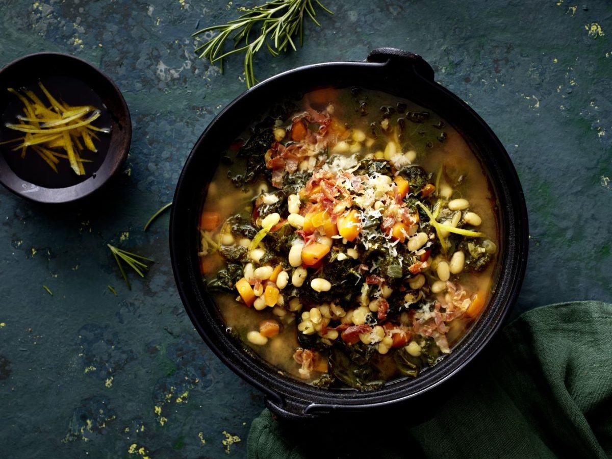 Toskanische Ribollita mit Bohnen in einer schwarzen Schüssel auf schwarzem Hintergrund.