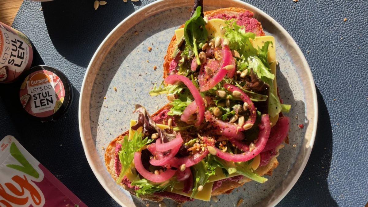 Bunt belegtes Brot mit Rote-Bete-Aufstrich, Käse, frischem Salat, eingelegten Zwiebeln und Sonnenblumenkernen auf Keramikteller.
