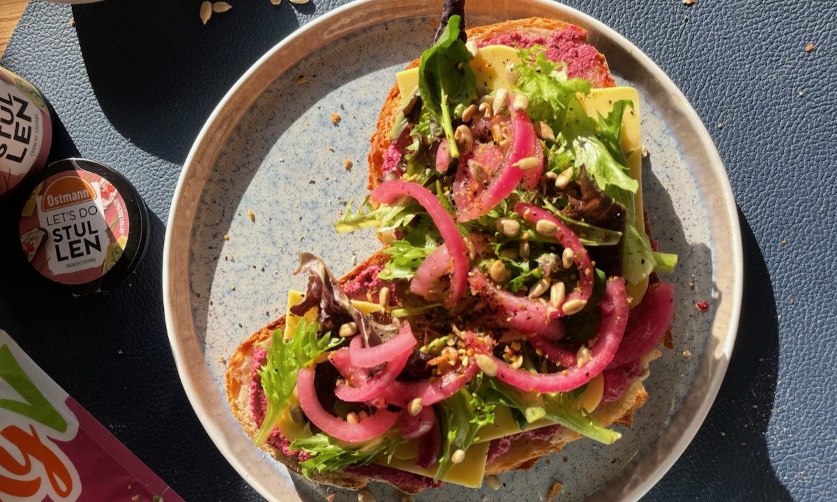 Bunt belegtes Brot mit Rote-Bete-Aufstrich, Käse, frischem Salat, eingelegten Zwiebeln und Sonnenblumenkernen auf Keramikteller.