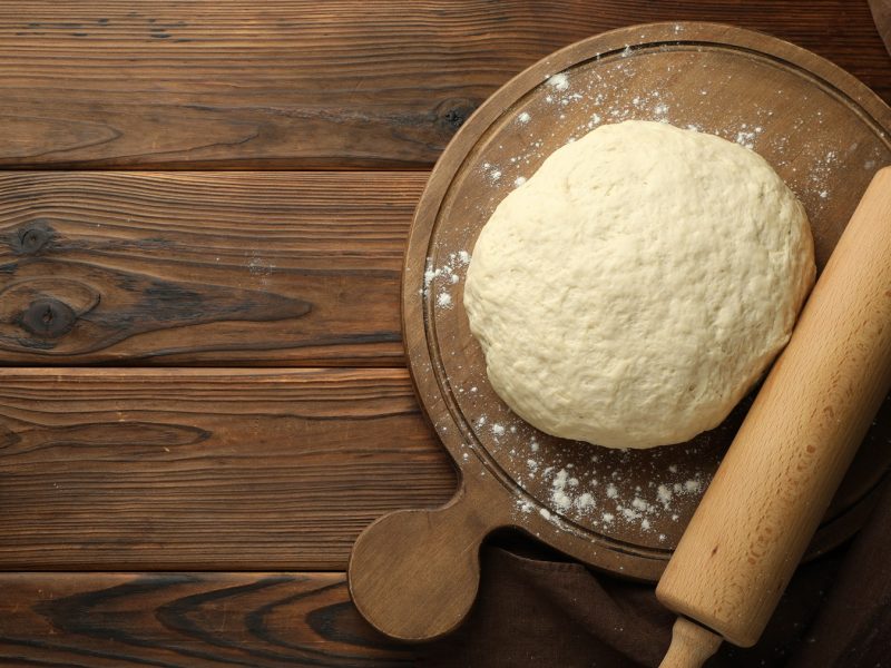 Draufsicht auf einen High-Protein-Teig auf einem Brettchen, daneben ein Nudelholz.