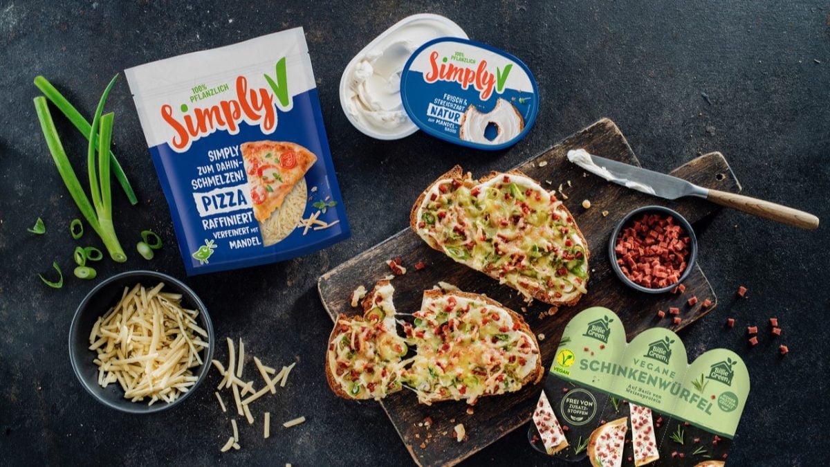 Vegane Flammkuchen-Stulle mit geschmolzenem Käse, Frühlingszwiebeln und Schinkenwürfeln neben Simply V und Billie Green Produkten.
