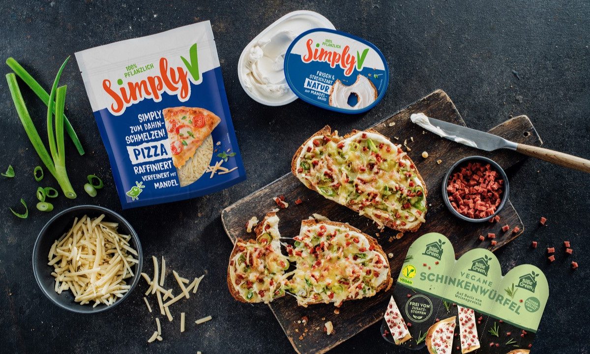 Vegane Flammkuchen-Stulle mit geschmolzenem Käse, Frühlingszwiebeln und Schinkenwürfeln neben Simply V und Billie Green Produkten.
