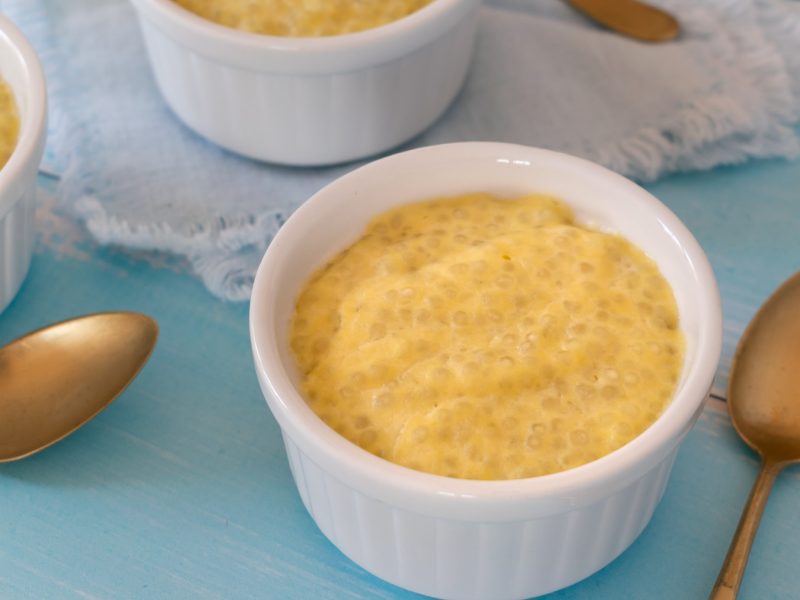 Drei weiße Schälchen mit dem Tapioka Pudding auf einem hellblauen Tisch mit goldenen Löffeln.