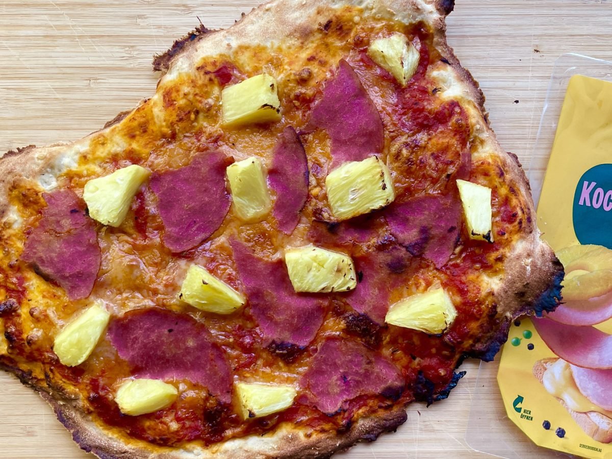 Selbstgemachte vegane Pizza Hawaii mit pflanzlichem Schinken und saftiger Ananas auf hellem Holzuntergrund.
