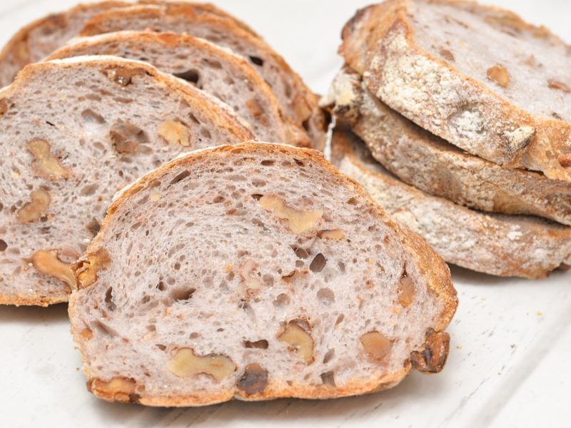 Draufsicht: Weißer Untergrund aus Holz, mehrere Scheiben Walnuss-Baguette.