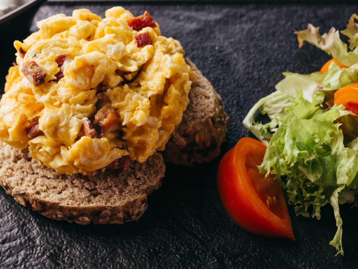 Zwei Scheiben Körnerbrot belegt mit DDR-Kultgericht "Affenfett", daneben frischer Salat mit Tomatenscheiben.