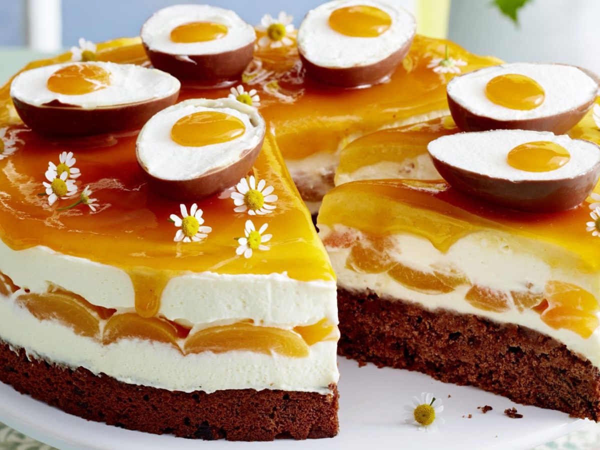 Saftige Aprikosen-Schmand-Torte mit Schokoboden, Sahnecreme und Aprikosenguss, dekoriert mit Schoko-Ostereiern und weißen Gänseblümchen.