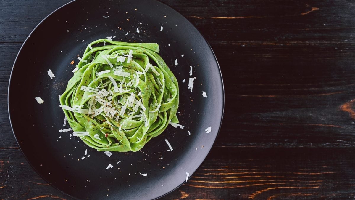 Draufsicht: Ein schwarzer Teller auf einem dunklen Untergrund mit selbst gemachten Bärlauch-Tagliatelle.