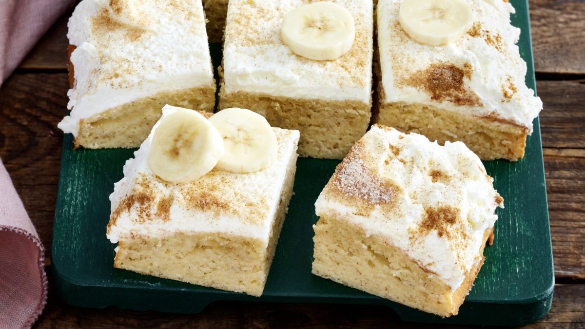 Mehrere Stücke vom Bananen-Skyr-Kuchen auf einem dunkelgrünen Teller und dunklem Holztisch. Alles von schräg oben fotografiert.