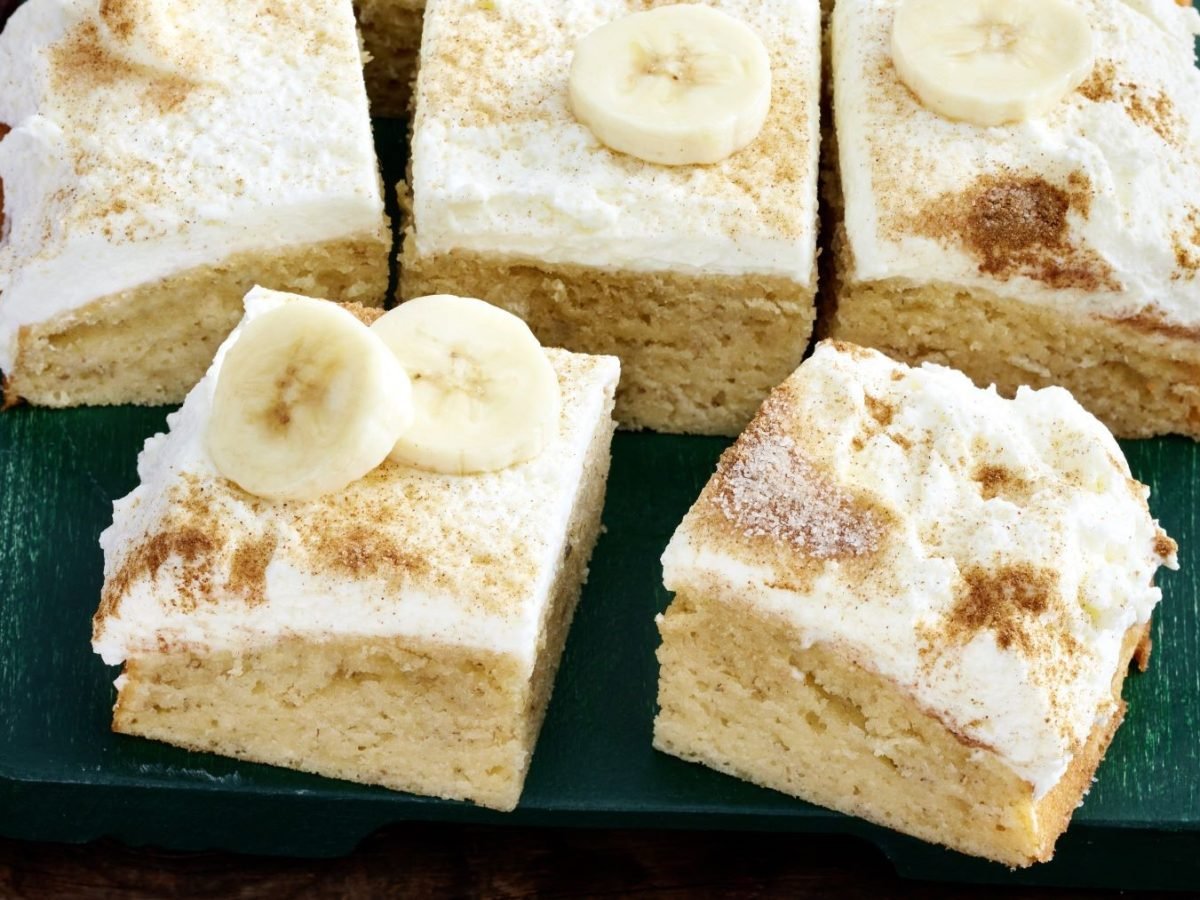 Mehrere Stücke vom Bananen-Skyr-Kuchen auf einem dunkelgrünen Teller und dunklem Holztisch. Alles von schräg oben fotografiert.