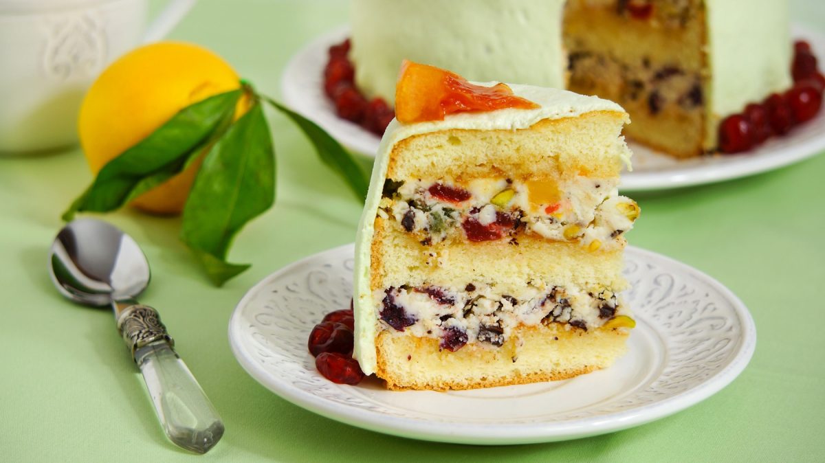 Ein saftiges Stück italienische Cassata mit grünem Überzug und Orangenstück, daneben ein Löffel und eine frische Zitrone.
