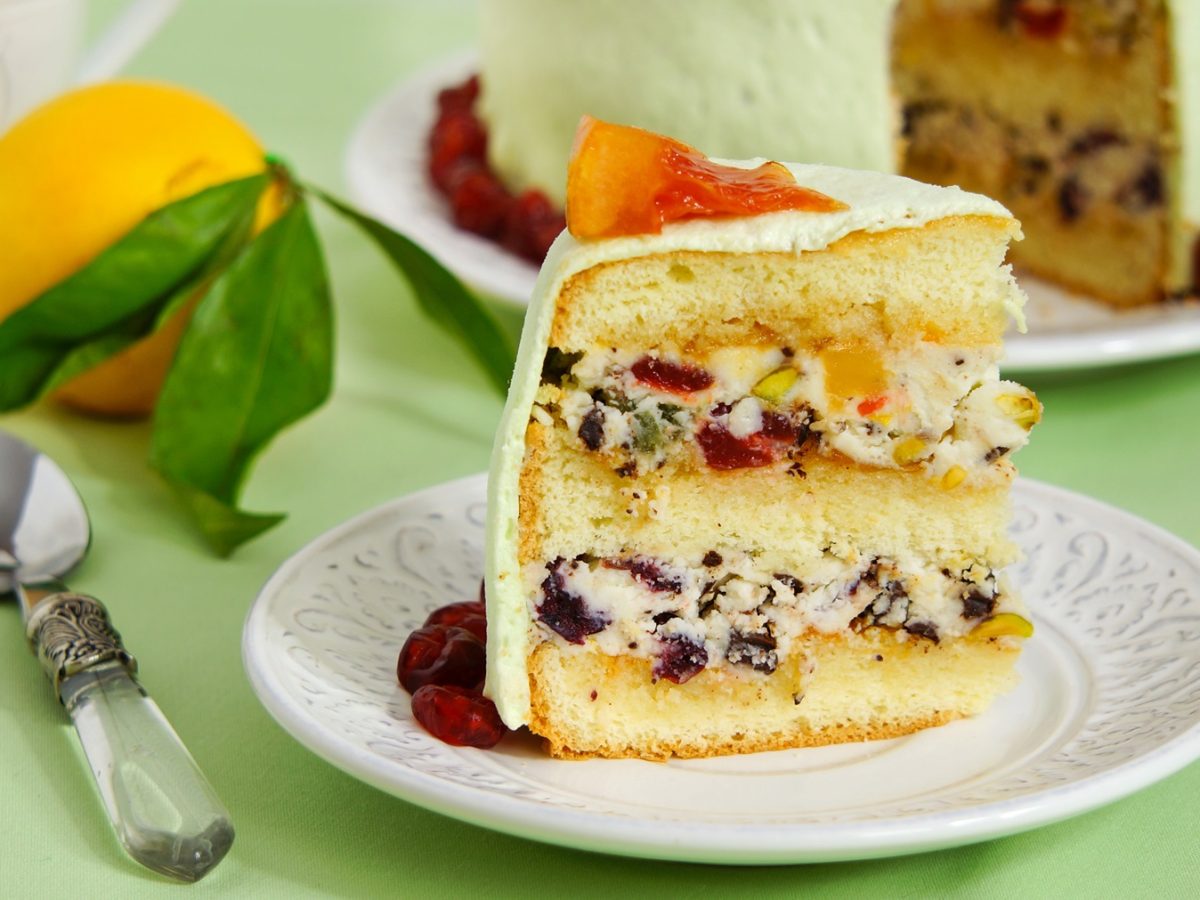 Ein saftiges Stück italienische Cassata mit grünem Überzug und Orangenstück, daneben ein Löffel und eine frische Zitrone.