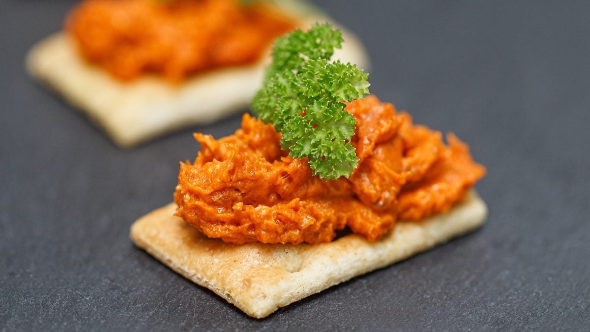 Draufsicht, schräg: Auf dunklem Untergrund liegen zwei Knäckebrote die mit einem Aufstrich aus rohem Fleisch bestrichen sind. Sie sind mit etwas frischer Petersilie garniert.