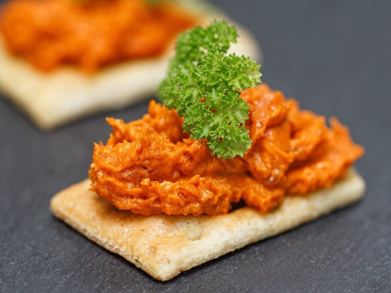 Draufsicht, schräg: Auf dunklem Untergrund liegen zwei Knäckebrote die mit einem Aufstrich aus rohem Fleisch bestrichen sind. Sie sind mit etwas frischer Petersilie garniert.
