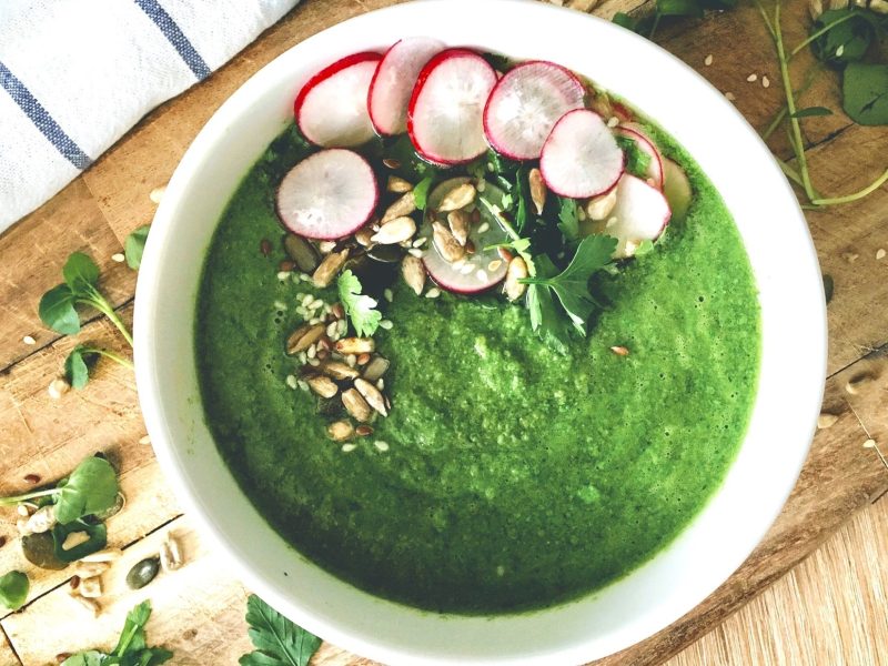 Draufsicht: Eine runde helle Schüssel mit einen Gemüsesuppe. Die ist mit Radieschen sowie Nüssen und Samen garniert.