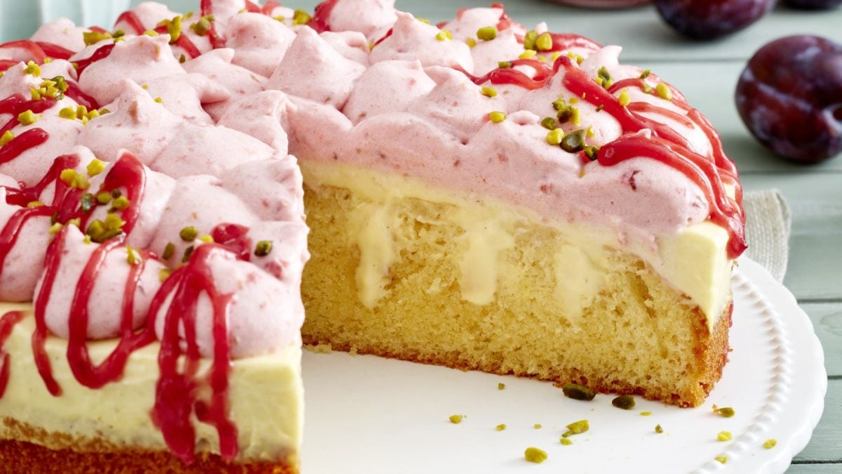 Draufsicht, schräg: Ein relativ flacher Kuchen, der auf einem hellen runden Untergrund liegt. Der Kuchen ist angeschnitten.