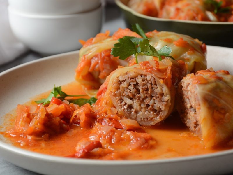 Frontal: Ein Teller auf dem zwei angeschnittene Kohlrouladen in einer Tomatensauce liegen.