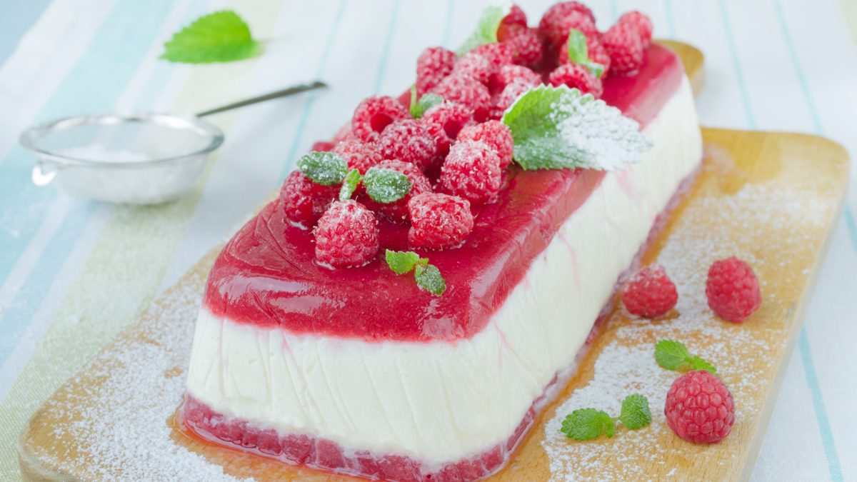 Das Semifreddo auf einem Holzbrett und hellblauem Holztisch. Alles von schräg oben fotografiert.