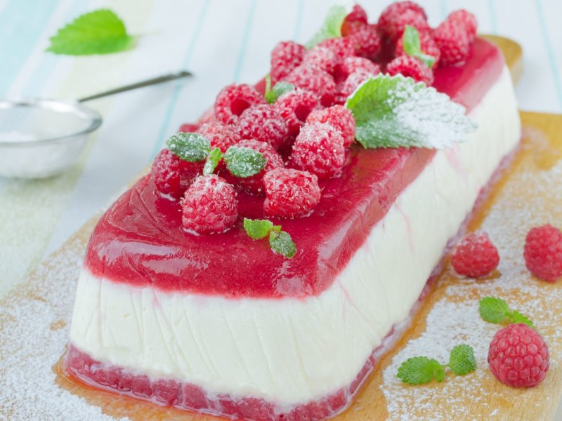 Das Semifreddo auf einem Holzbrett und hellblauem Holztisch. Alles von schräg oben fotografiert.