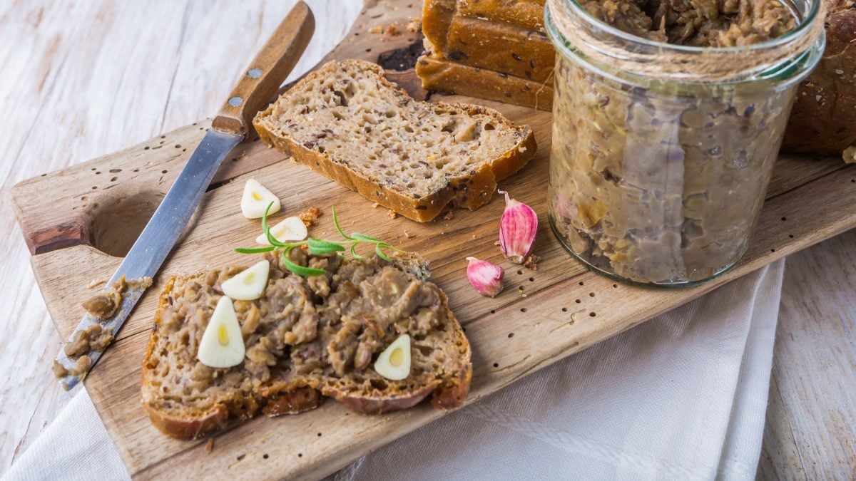 Eine Brotscheibe mit dem Linsenaufstrich auf einem hellen Untergrund von schräg oben fotografiert.
