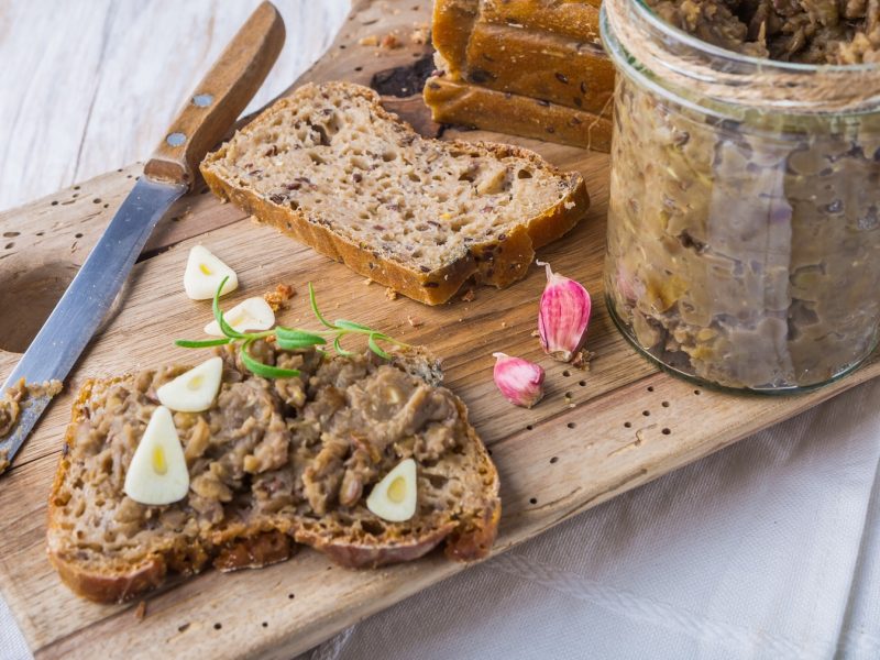 Eine Brotscheibe mit dem Linsenaufstrich auf einem hellen Untergrund von schräg oben fotografiert.