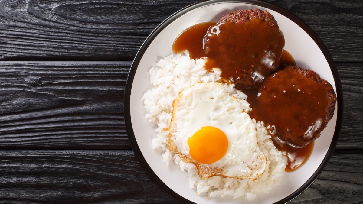 Ein weißer Teller mit dem Gericht Loco Moco auf schwarzem Holzuntergrund. Alles direkt von oben fotografiert.