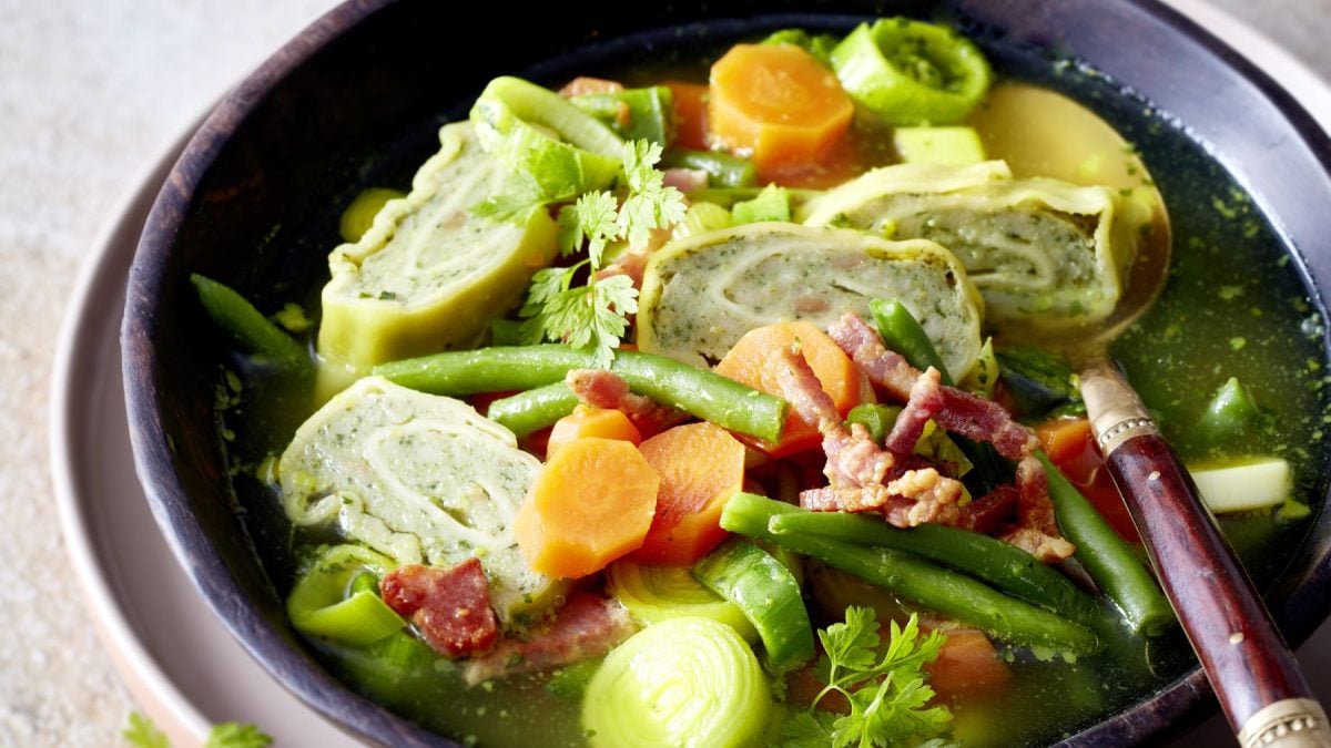 Bunte Suppe mit geschnittenen Maultaschen, Möhren, grünen Bohnen, Lauch und Speck, angerichtet in rustikaler Schale.