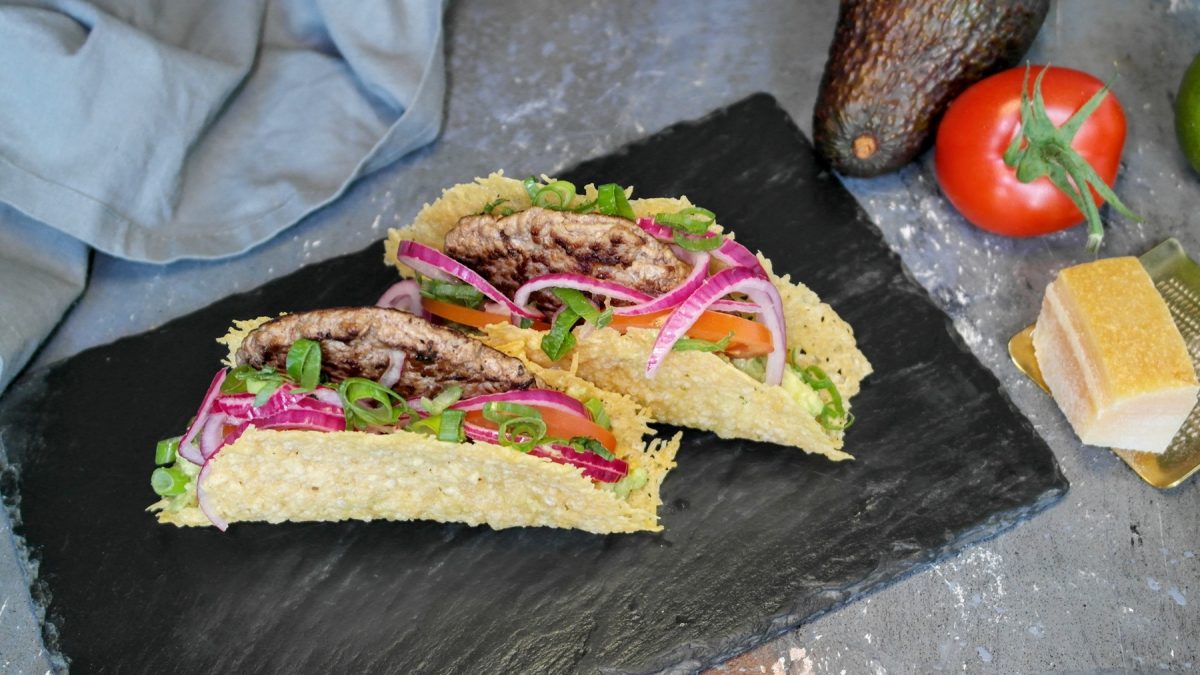 Zwei Parmesan-Tacos auf einer schwarzen Schiefertafel und grauem Steintisch. Alles von schräg oben fotografiert.