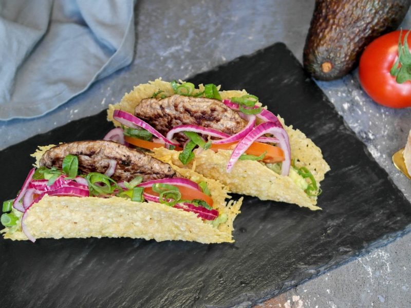 Zwei Parmesan-Tacos auf einer schwarzen Schiefertafel und grauem Steintisch. Alles von schräg oben fotografiert.
