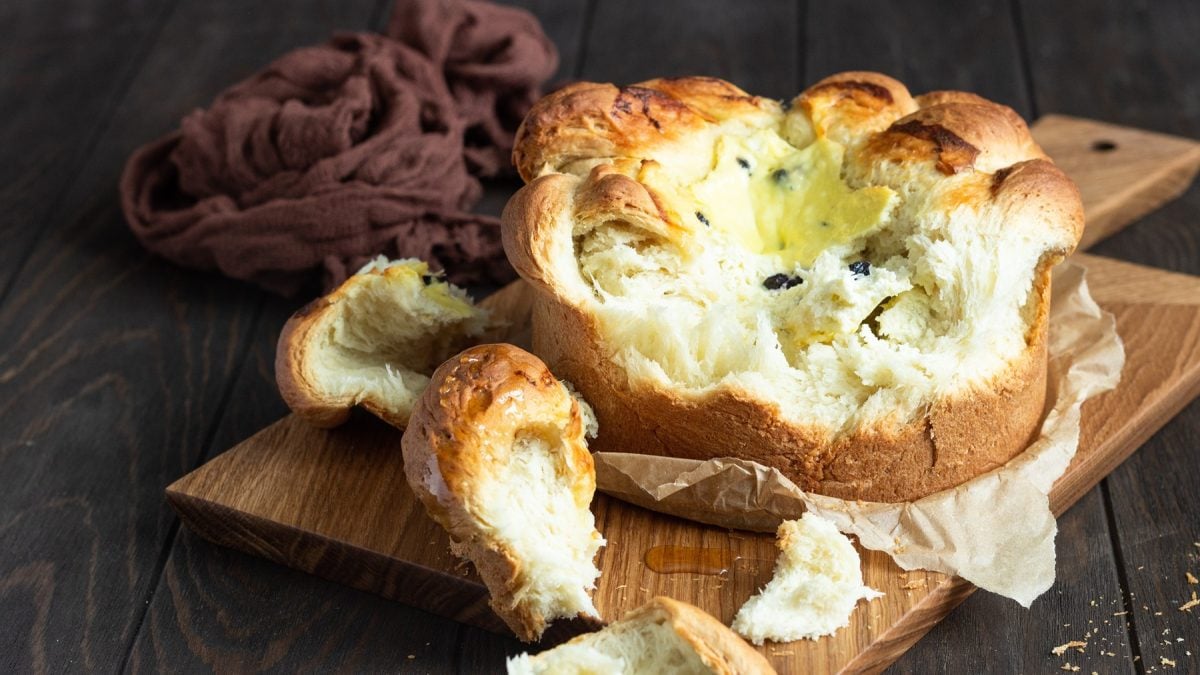 Goldbraune, weiche Pasca mit zarter Füllung und Teigstücken auf dunklem Holztisch und zerknittertem Tuch.