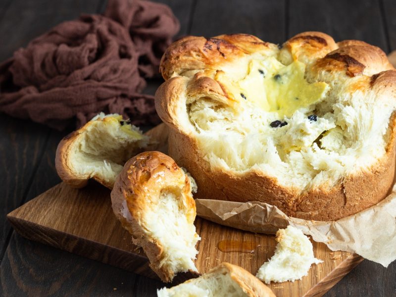 Goldbraune, weiche Pasca mit zarter Füllung und Teigstücken auf dunklem Holztisch und zerknittertem Tuch.