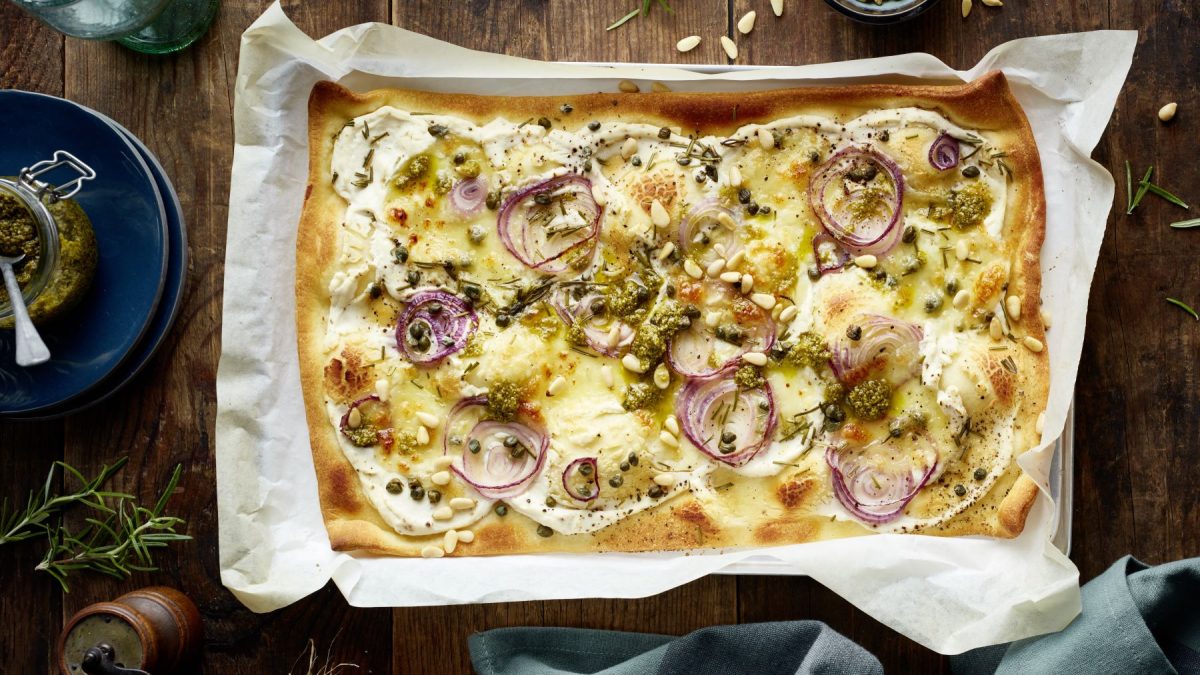 Die Pizza Bianca auf einem Backblech und dunklem Untergrund. Alles direkt von oben fotografiert.