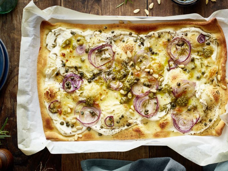 Die Pizza Bianca auf einem Backblech und dunklem Untergrund. Alles direkt von oben fotografiert.