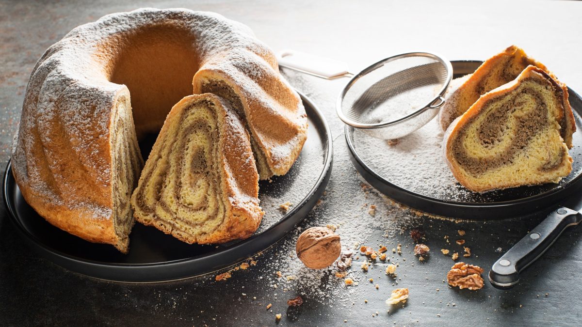 Saftige Potica mit aromatischer Nussfüllung, serviert mit Puderzucker und Walnüssen auf dunkler Tischplatte.