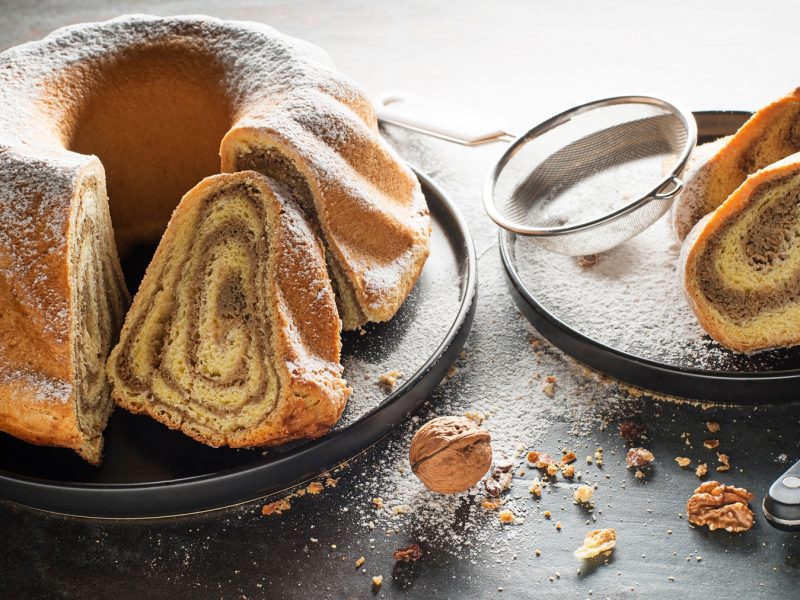 Saftige Potica mit aromatischer Nussfüllung, serviert mit Puderzucker und Walnüssen auf dunkler Tischplatte.