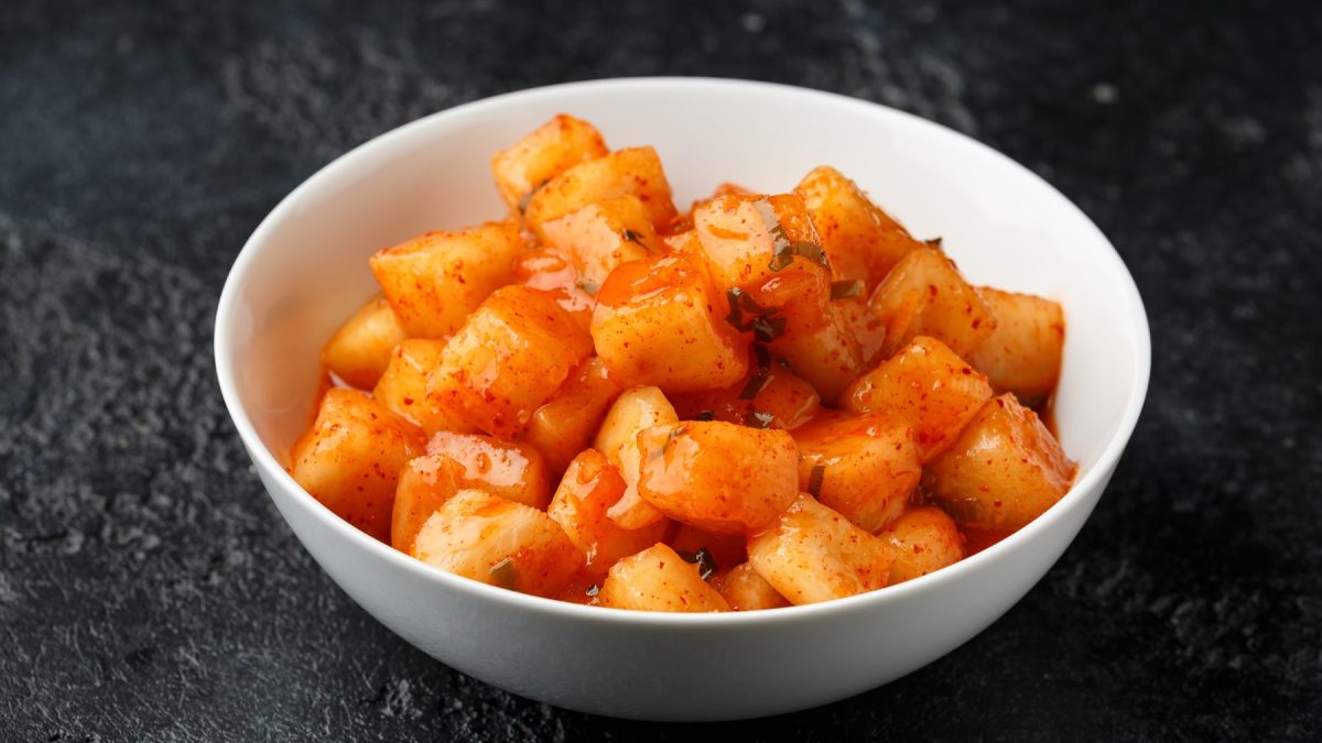 Ein weißes Schälchen mit dem Rettich Kimchi auf einem dunklen Untergrund. Alles nah und von der Seite fotografiert.