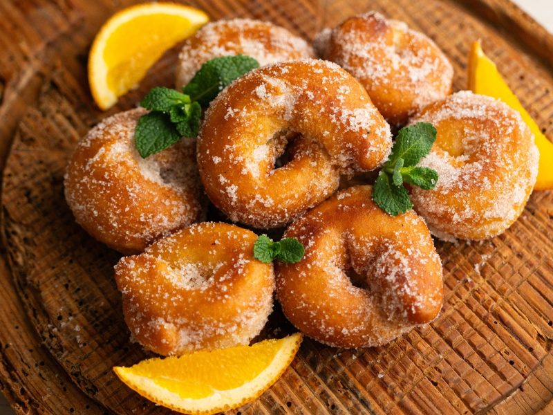 Zuckerbestäubte Rosquillas mit frischer Minze und Orangenstücken auf einem rustikalen Holztablett.