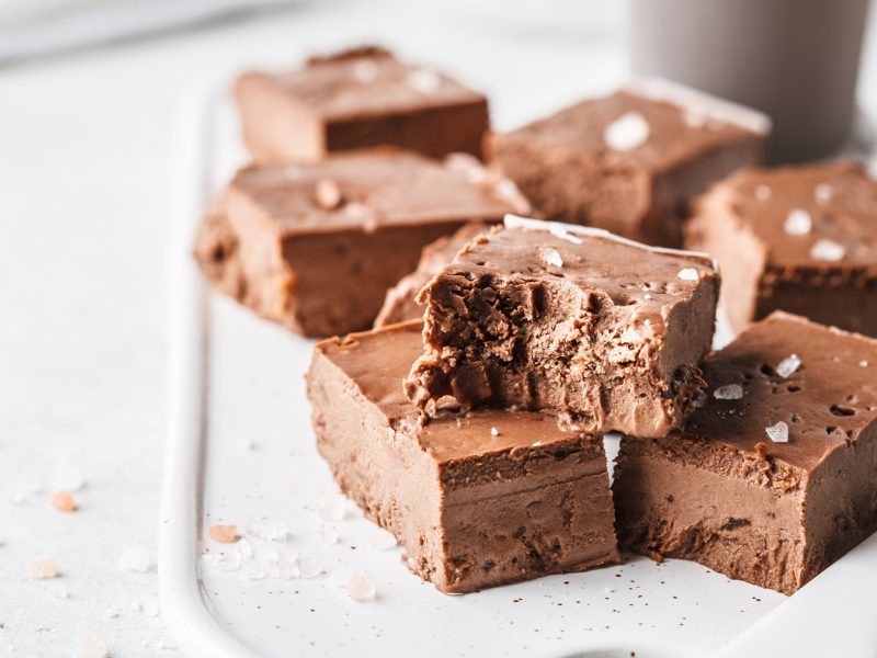 Schokoladige Fudge-Stücke mit zarter Textur und Salzflocken liegen verführerisch auf einer weißen Keramikplatte.