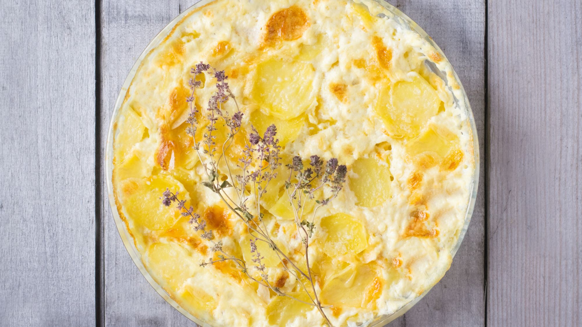 Überbackene Kartoffelröschen in cremiger Béchamelsauce mit goldbrauner Kruste in rechteckiger Auflaufform auf Bastuntersetzer.