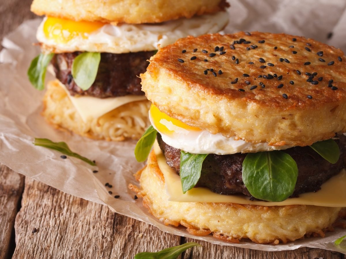 Zwei Blumenkohl-Burger auf einem dunklen Holztisch mit hellem Backpapier.