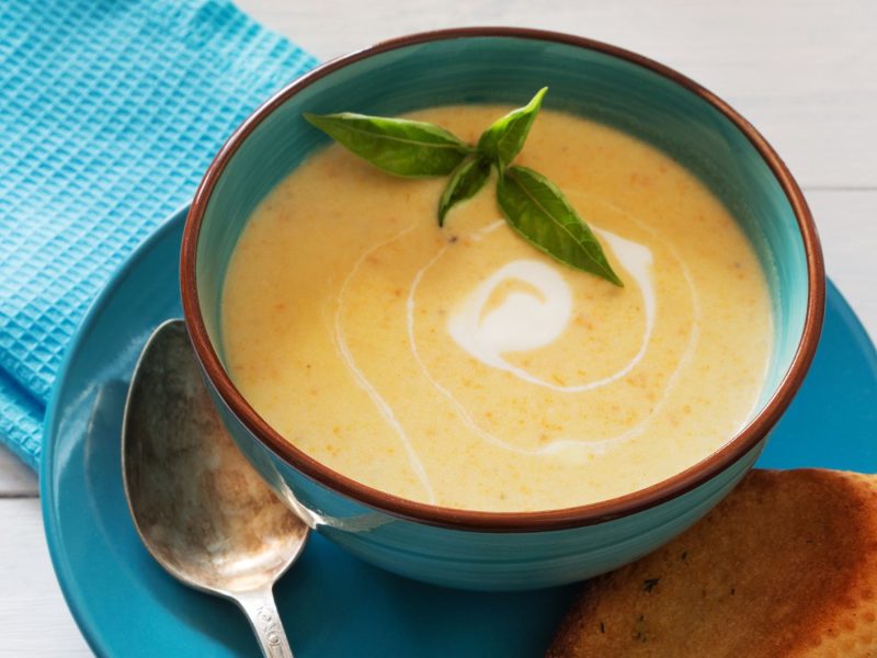 Cremige Buttermilch-Kartoffelsuppe mit Sahnewirbel und Basilikumblättern in türkisfarbener Schale auf blauer Serviette.